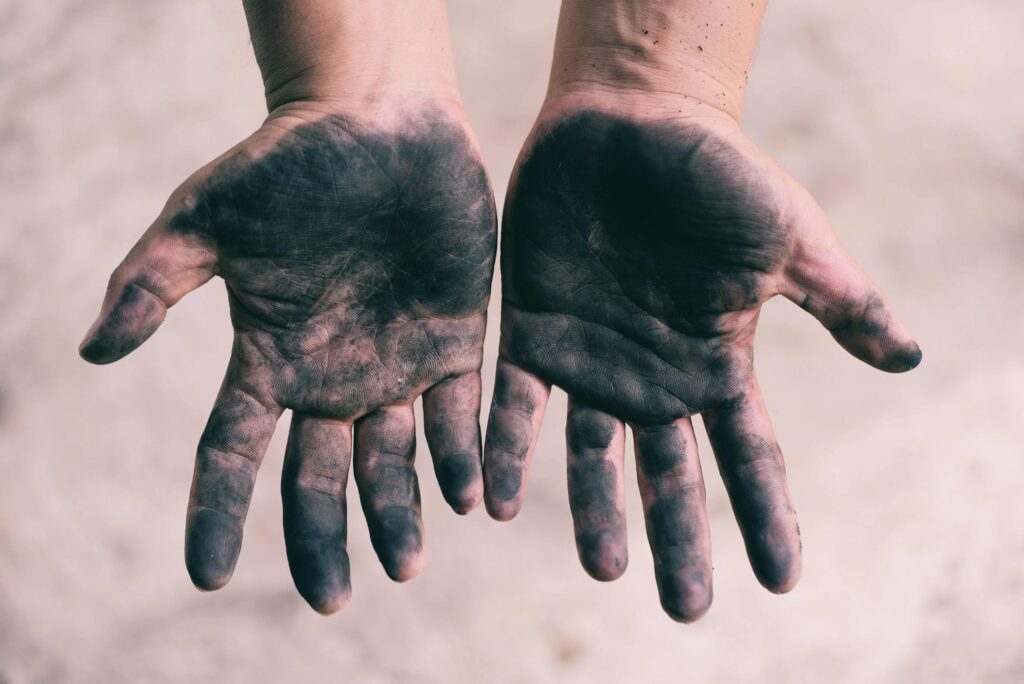 Dirty hands in focus against a blurred background, suggesting the person has just finished changing a flat tire on their car.