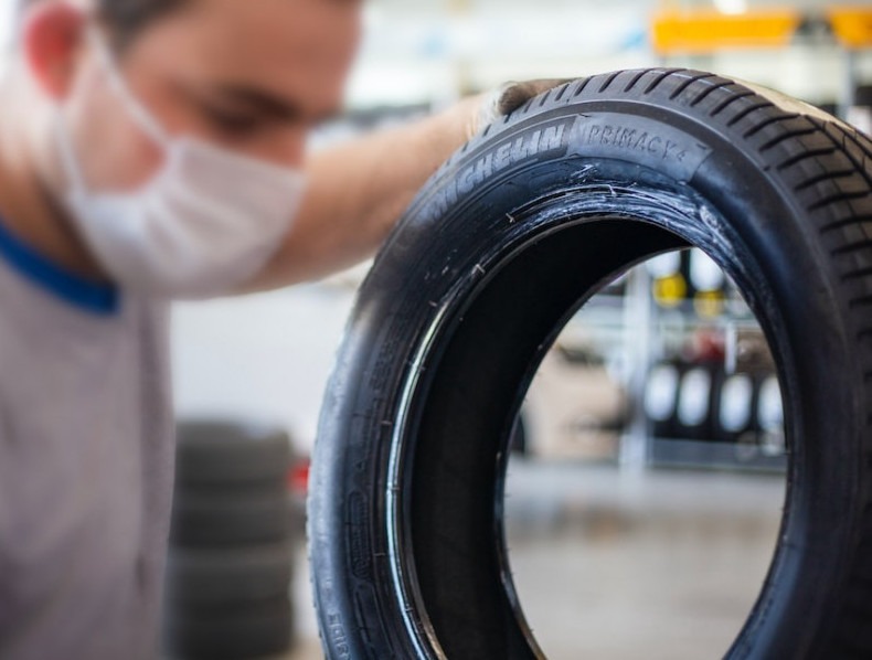 A technician wearing a face mask inspects a Michelin Primacy tire up close in a service shop. 