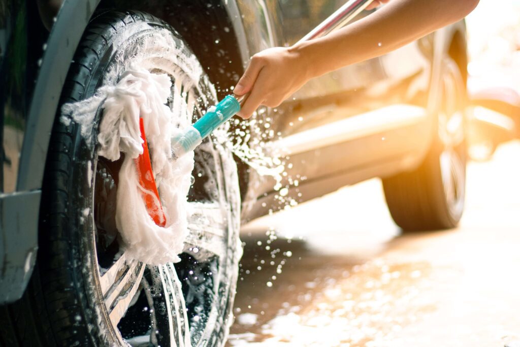 A person using a cleaning sponge to clean a tire. The tire is mounted on a car, suggesting that proper tire maintenance, such as cleaning, can help extend tire life. 