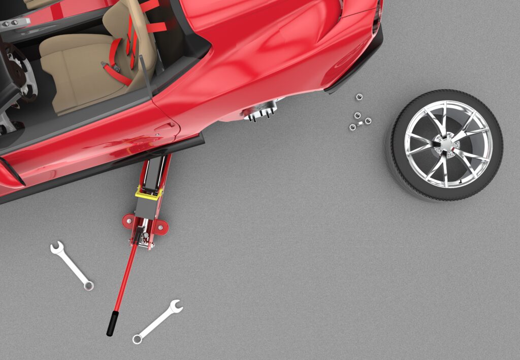 An artistic and realistic expression of a red cabrio with brown leather interior that is lifted by a car jack. The tire is removed from the car and is standing next to the car. The lug nuts are also near the tire. Some other tools can also be seen on the ground.