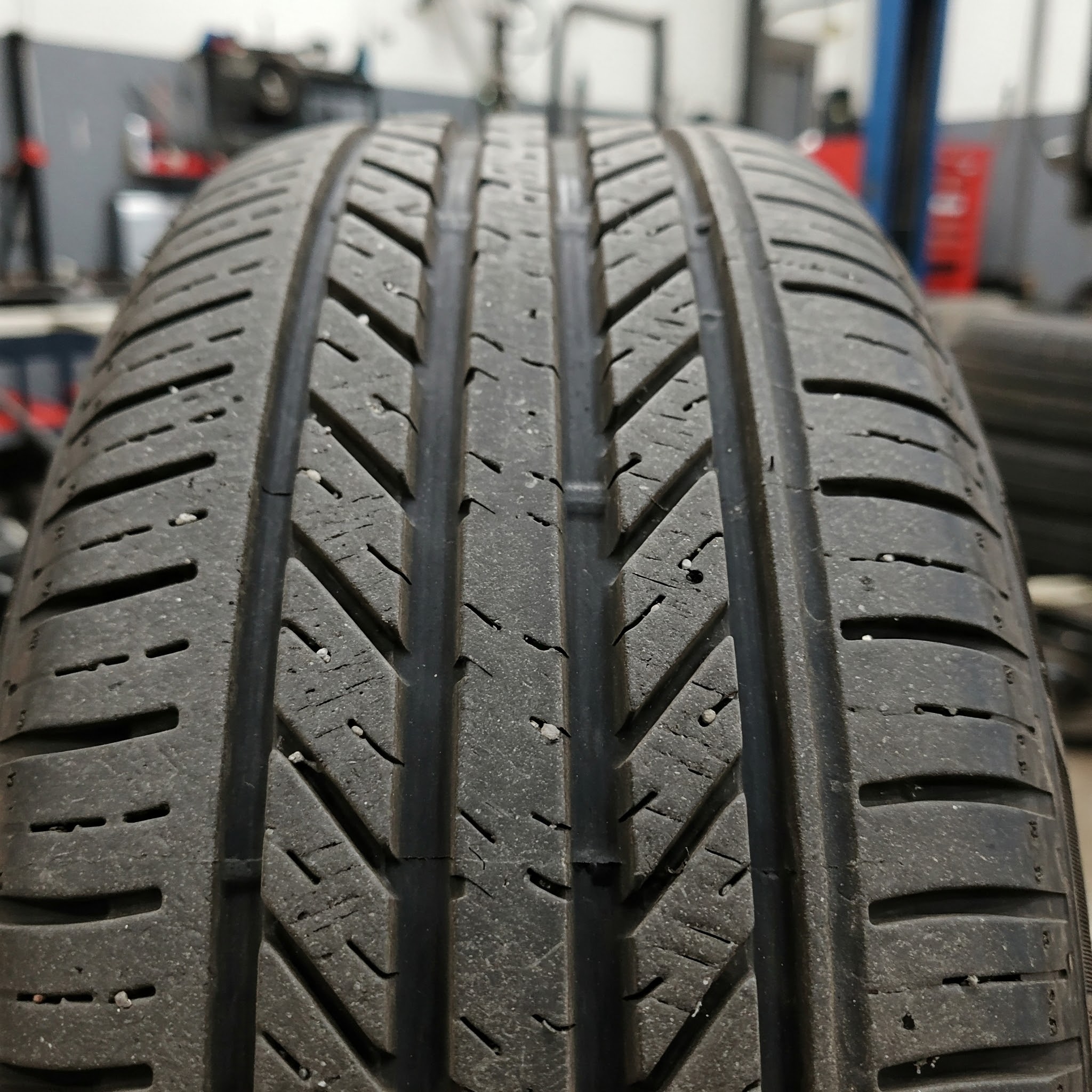 A detailed image of a tire with visible tire feathering. The tire is inside a garage, and some more equipment and tools can be seen in the background, which is blurry.