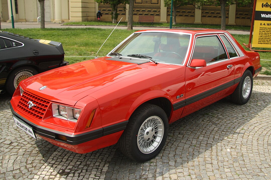A 1979 Ford Mustang photographed at Legendy 2019 in Prague. The car showcases a sleek and angular design typical of the early Fox-body generation, with a red paint job and clean lines that marked a departure from the Mustang II.