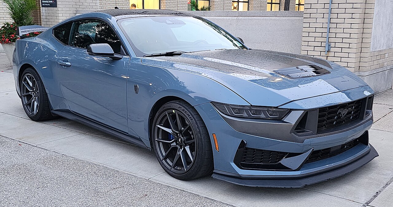 Side profile of the 2024 Ford Mustang Dark Horse, featuring a striking and aggressive exterior design. The car is finished in a dark metallic paint, with sharp body lines, a prominent rear spoiler, and unique Dark Horse badging that highlights its performance-focused identity.