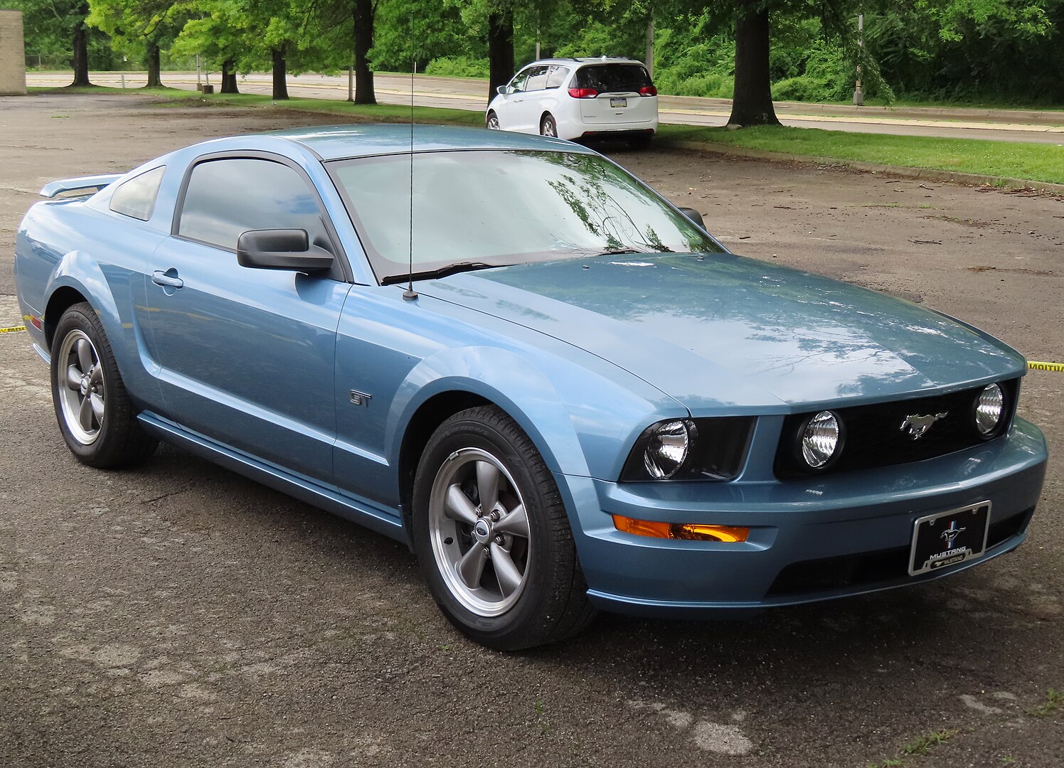 A 2005 Ford Mustang GT Deluxe Coupe, captured from the front-right angle, showcasing its retro-inspired design, iconic grille, and muscular stance. The car is parked in an outdoor setting, emphasizing its classic and timeless appeal.
