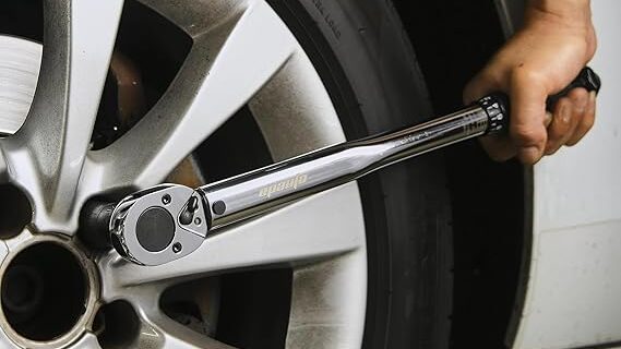 A person using a torque wrench to adjust their car wheel nut torque settings for proper tightening on an alloy wheel.