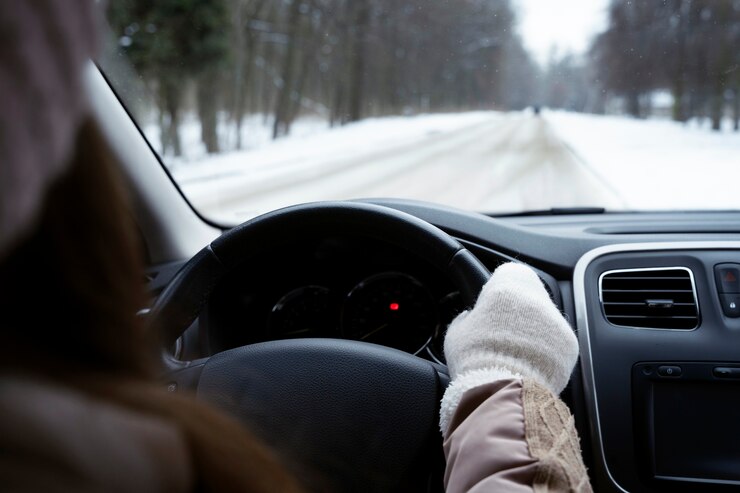 A woman driving her car on a snowy road. She is equipped with gloves as the temperature may be low, and she is concentrated on the road. 