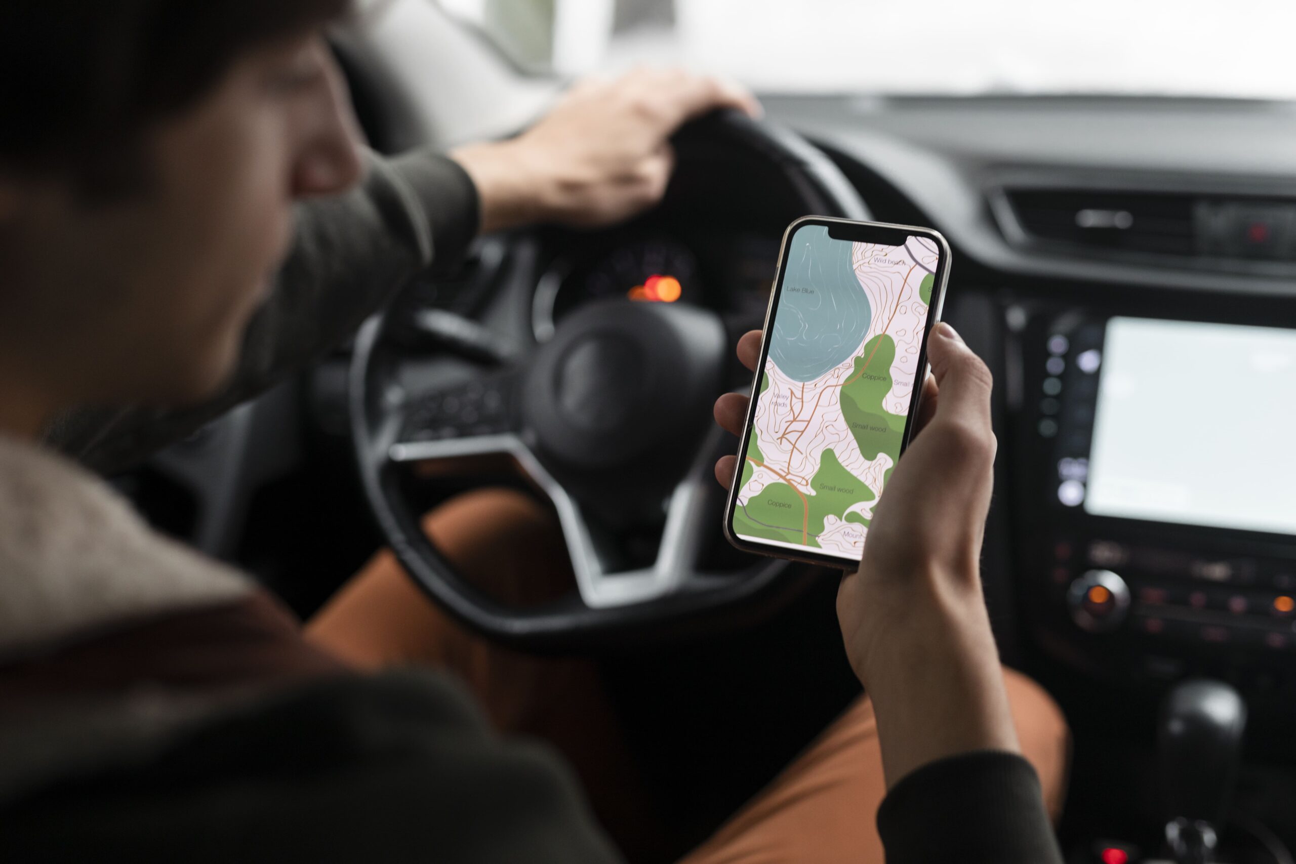 A driver consulting navigation app on smartphone while parked, showing the importance of proper route planning and using reliable navigation tools for road trips.