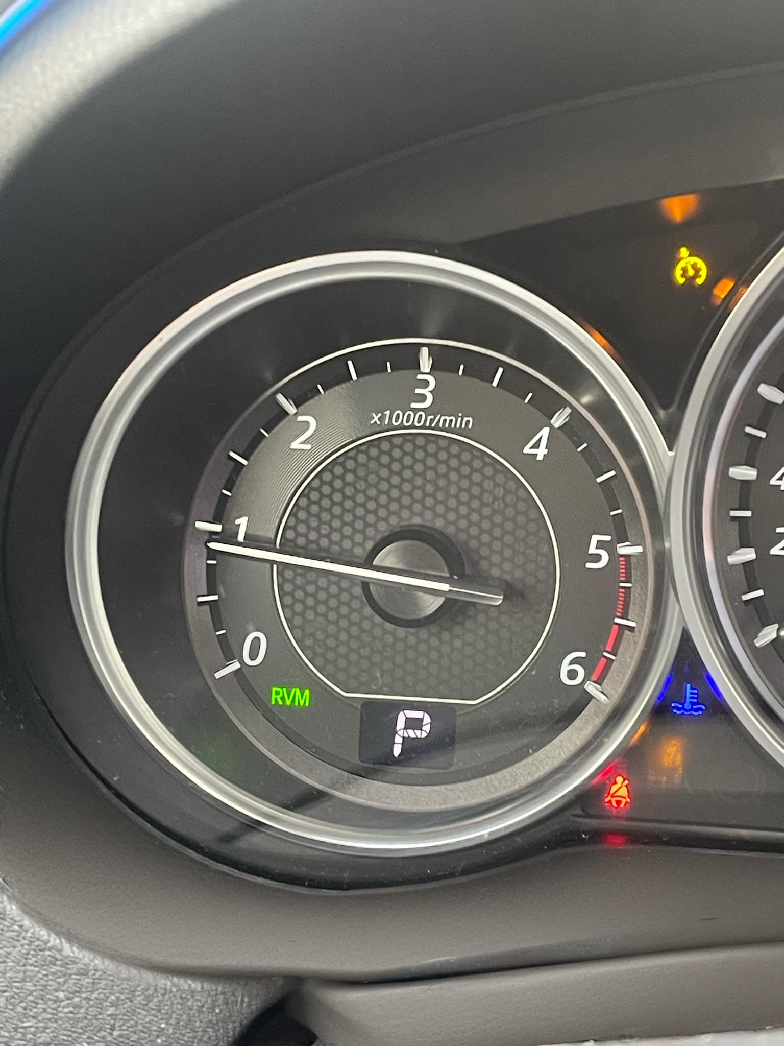 A close-up view of a car tachometer displaying RPM levels, with the needle resting just above 0 while the car is in park mode. This image highlights an idle engine, which can be related to diagnosing why the engine revs up and down while idling.