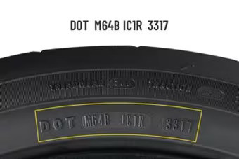 A close-up shot of a tire sidewall with a yellow curved rectangle highlighting the DOT code "DOT M64B IC1R 3317". The letters are embossed into the black rubber of the tire. Above the highlighted section, other faint tire markings like "TREADWEAR" and "TRACTION" are also visible on the sidewall. The image focuses on the texture and markings of the tire.