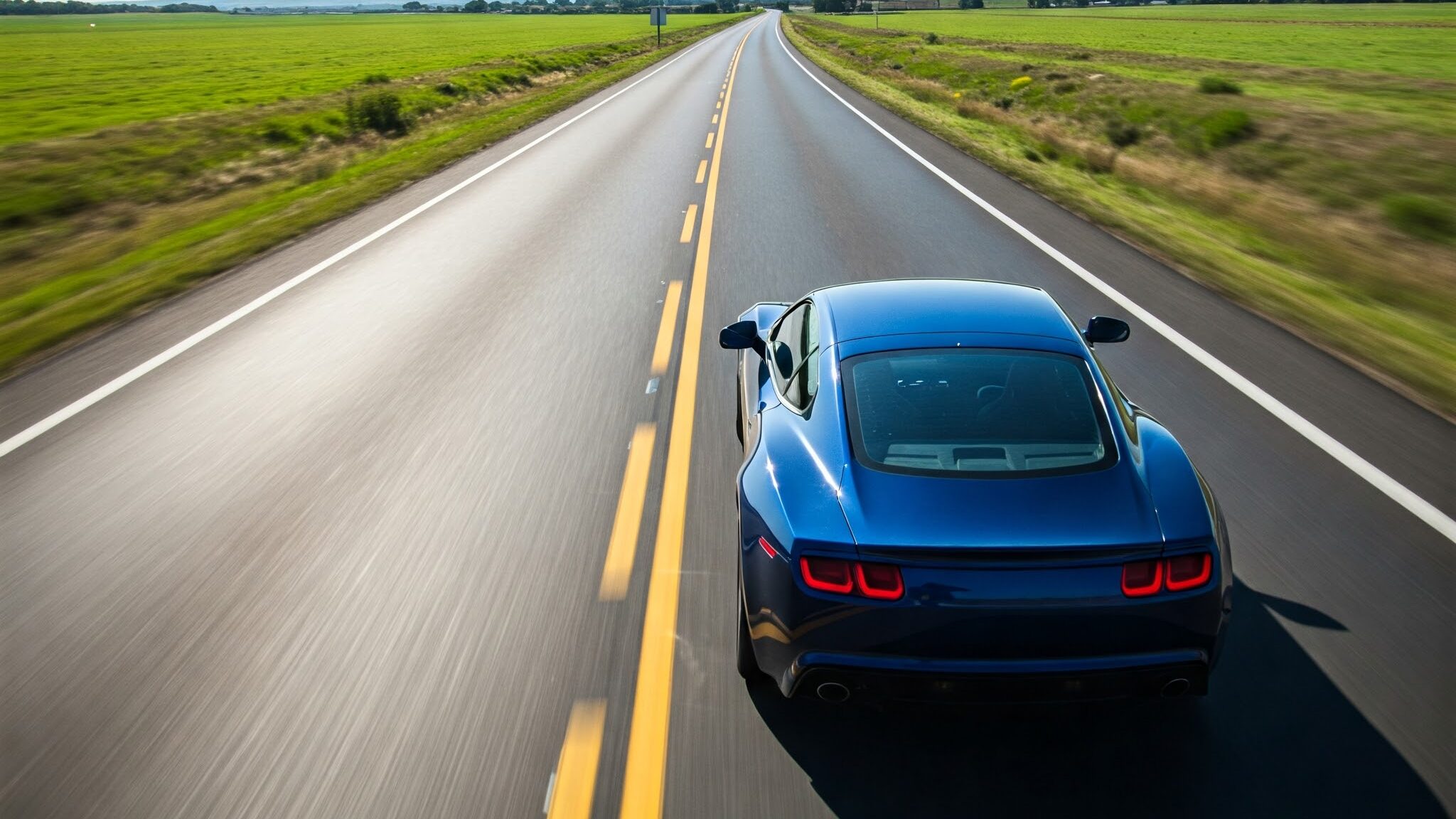 A blue modern car driving smoothly on a well-maintained road outside the city. The weather is sunny and everywhere around the road is green.