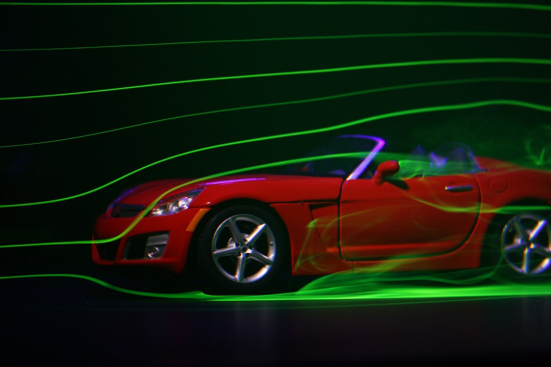 A red sports car without a roof on a black background and some green lines around it that represent aerodynamics and air passing over the car. 